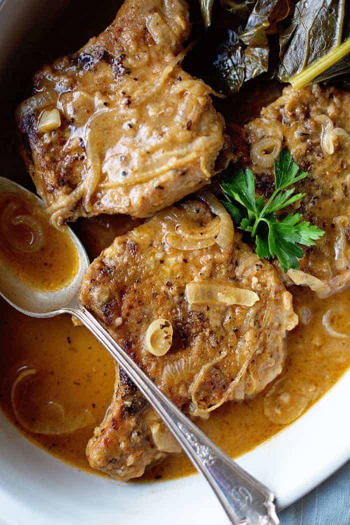 An overhead of Smothered Pork Chops in pork chop gravy in large bowl served with greens and a spoon