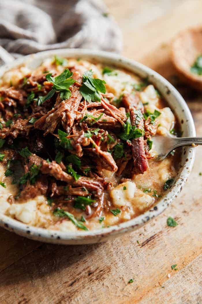 Mississippi Pot Roast made in a crockpot served over some garlic mashed potatoes with a fork to serve