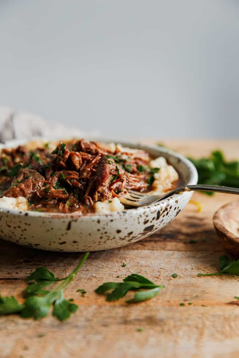 Brown Sugar Mississippi Pot Roast Recipe made in a crock pot sitting in a bowl over mashed potatoes