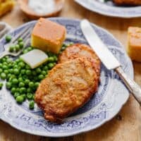 2 Southern Fried pork chops on blue plate with green peas, butter and cornbread