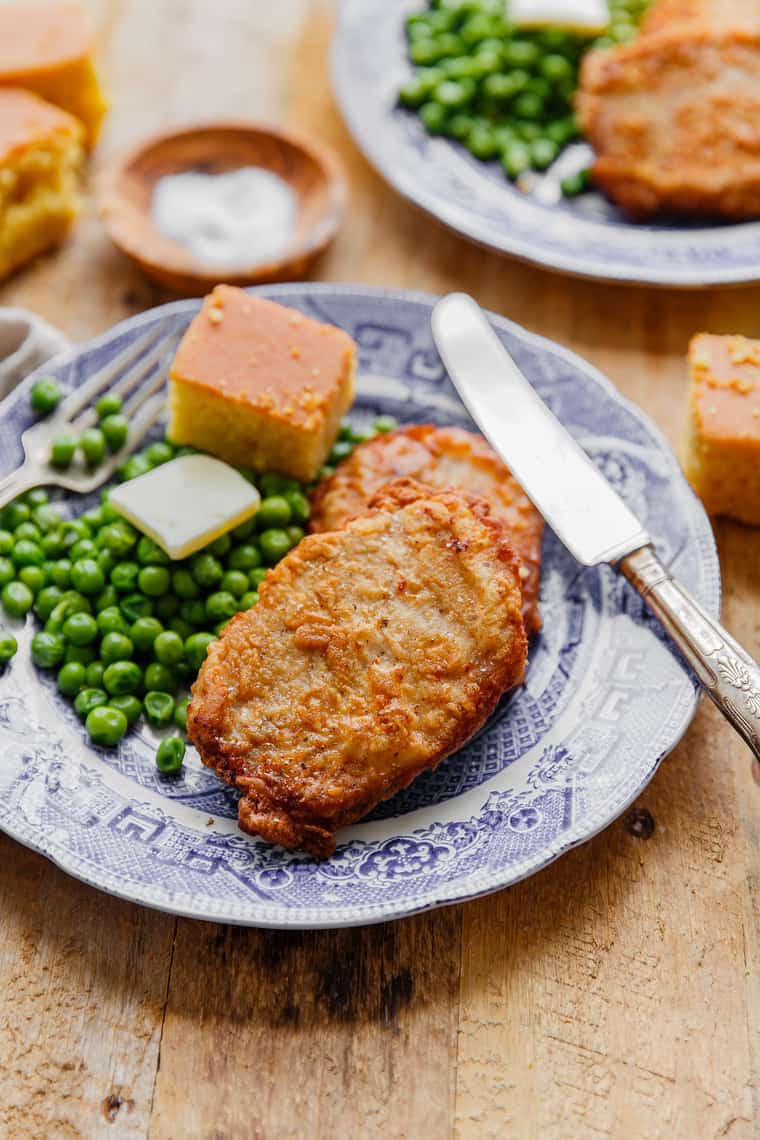 2 Southern Fried pork chops on blue plate with green peas, butter and cornbread