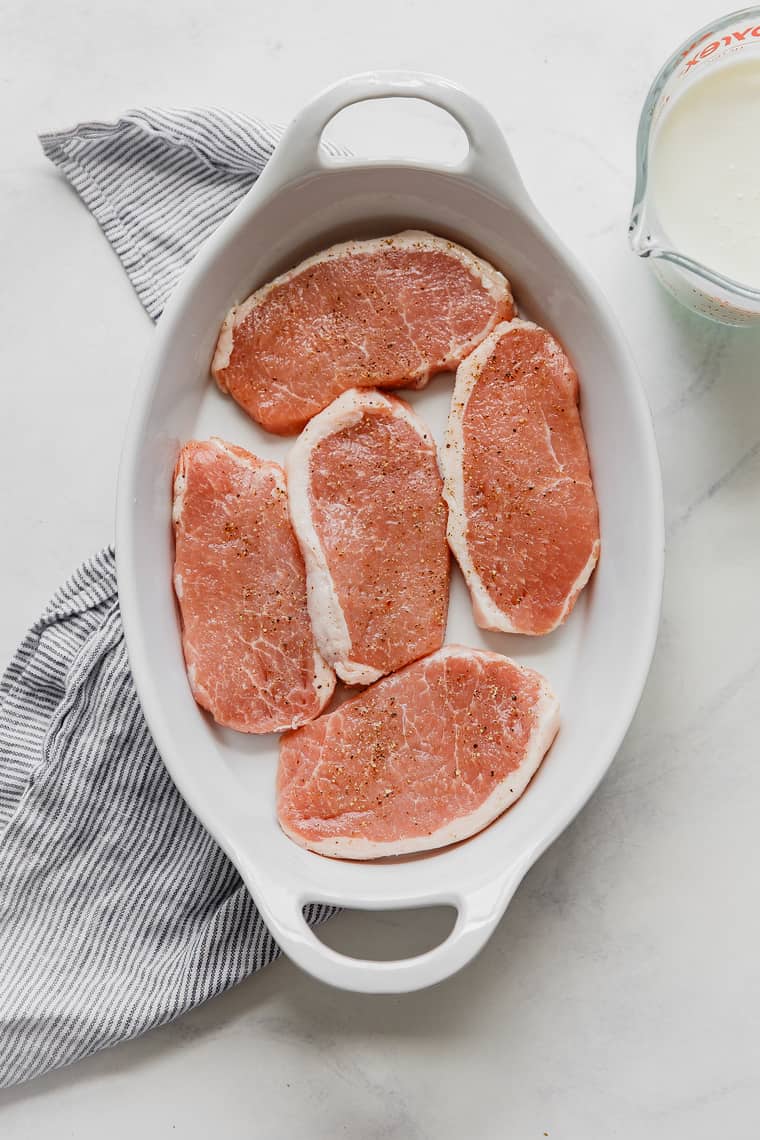 Raw seasoned pork chops resting in white bowl