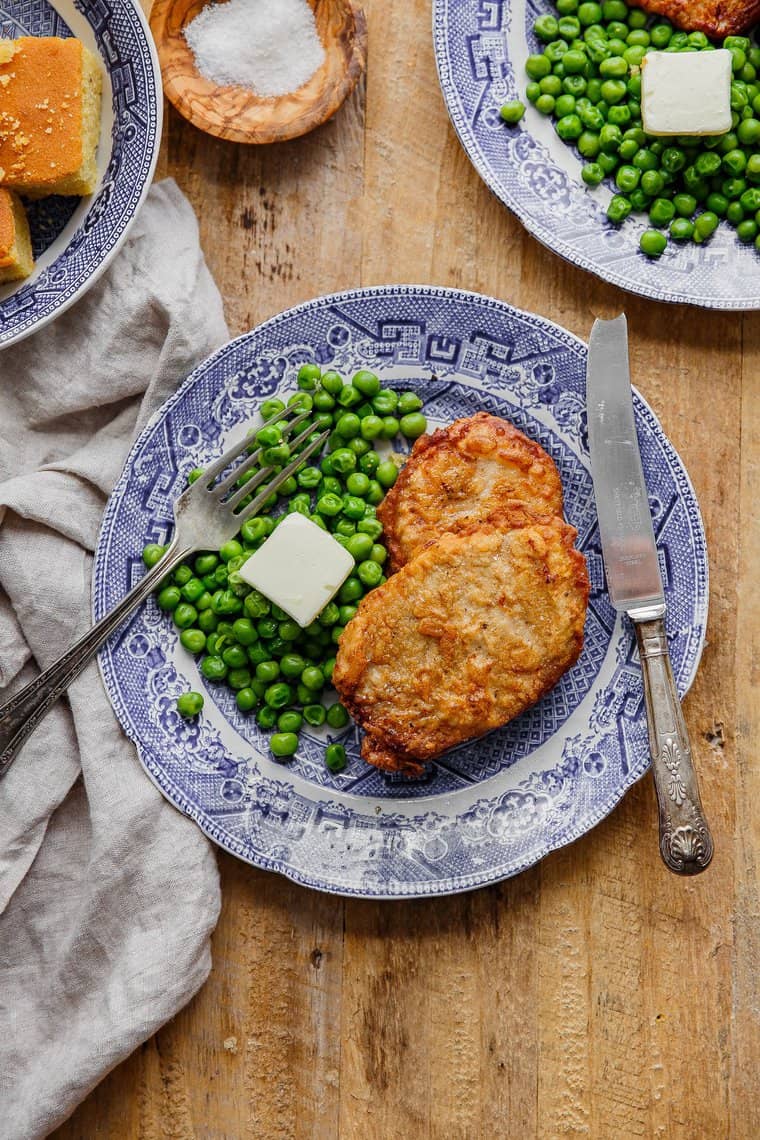 2 Southern Fried pork chops on blue plate with green peas and butter