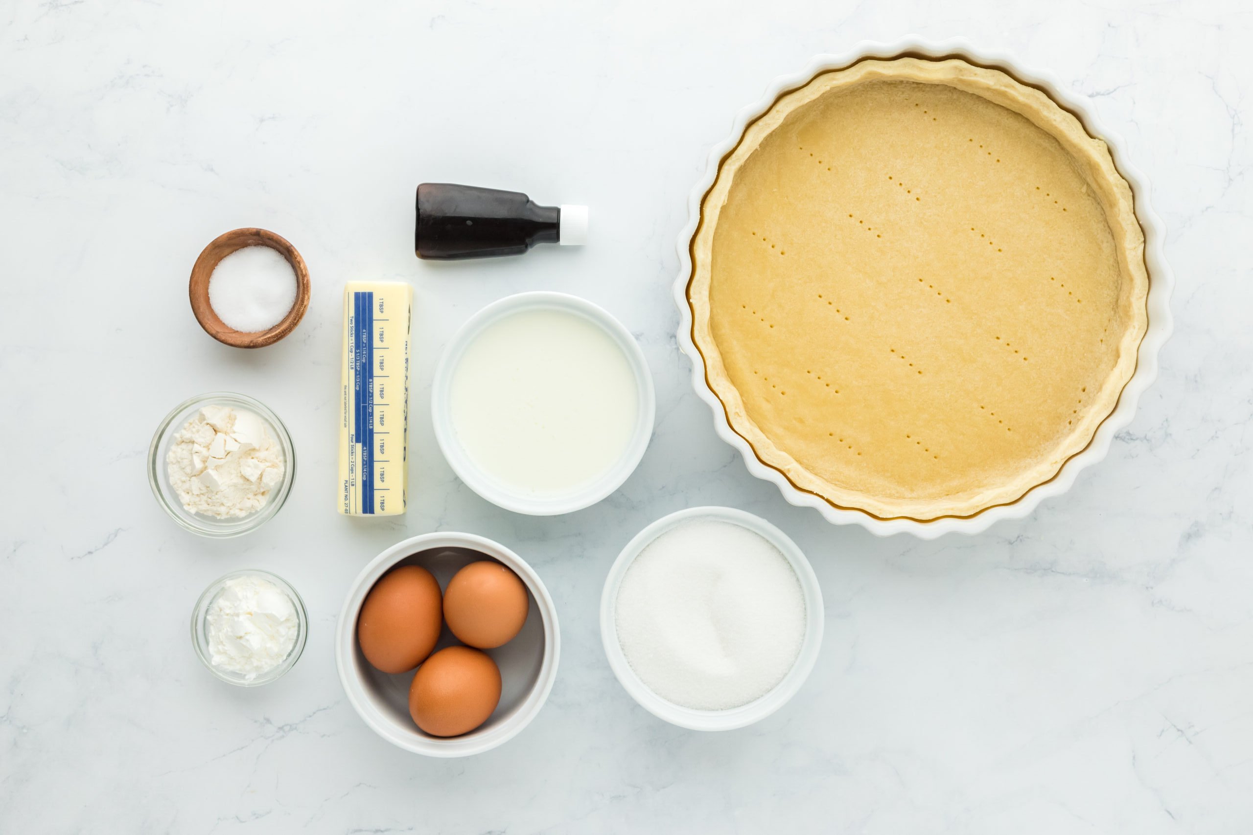 Pie crust, sugar, eggs, buttermilk, butter, vanilla, flour, cornstarch and salt in white bowls on white countertop