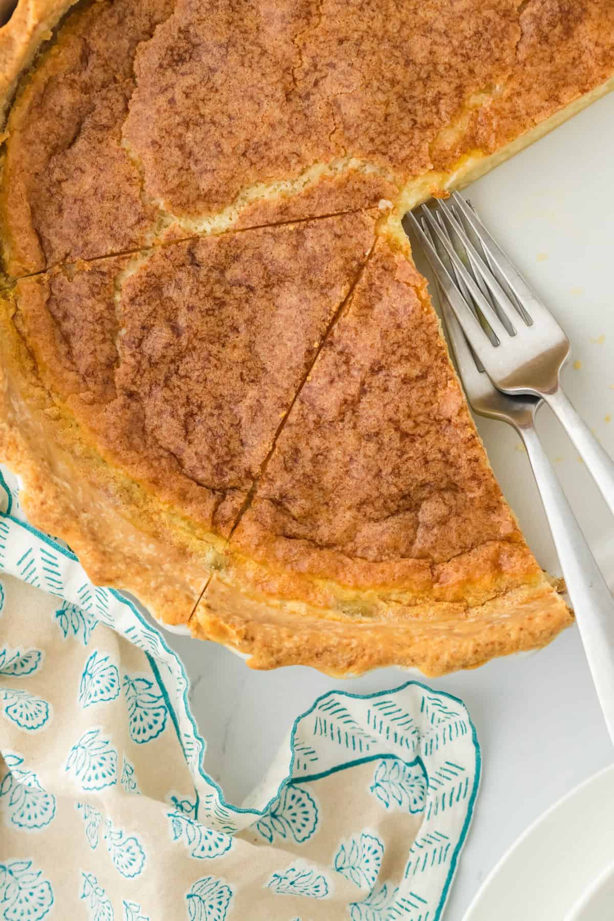 Sliced easy buttermilk pie recipe with two forks on the inside on white countertop with patterned blue napkin.