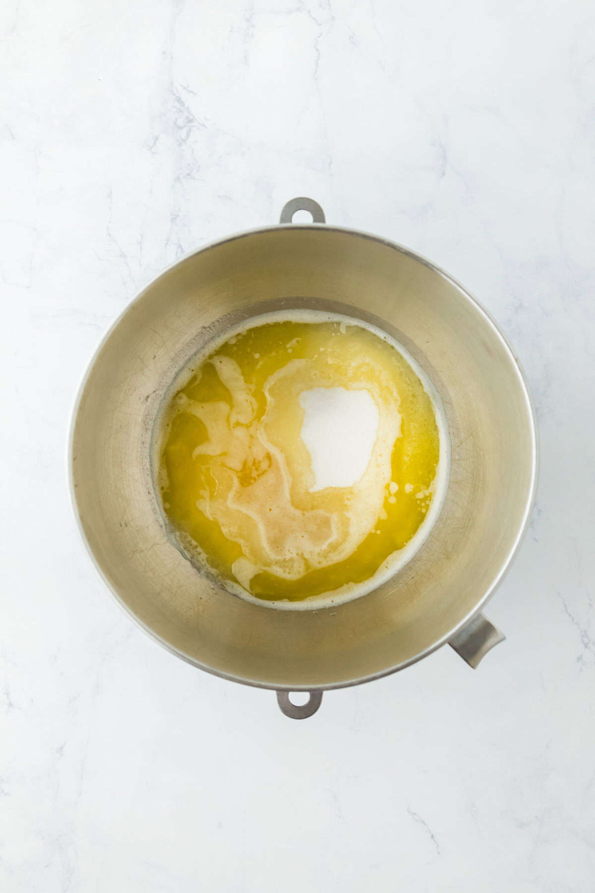 Melted butter and sugar added to a stand mixer bowl on a white countertop