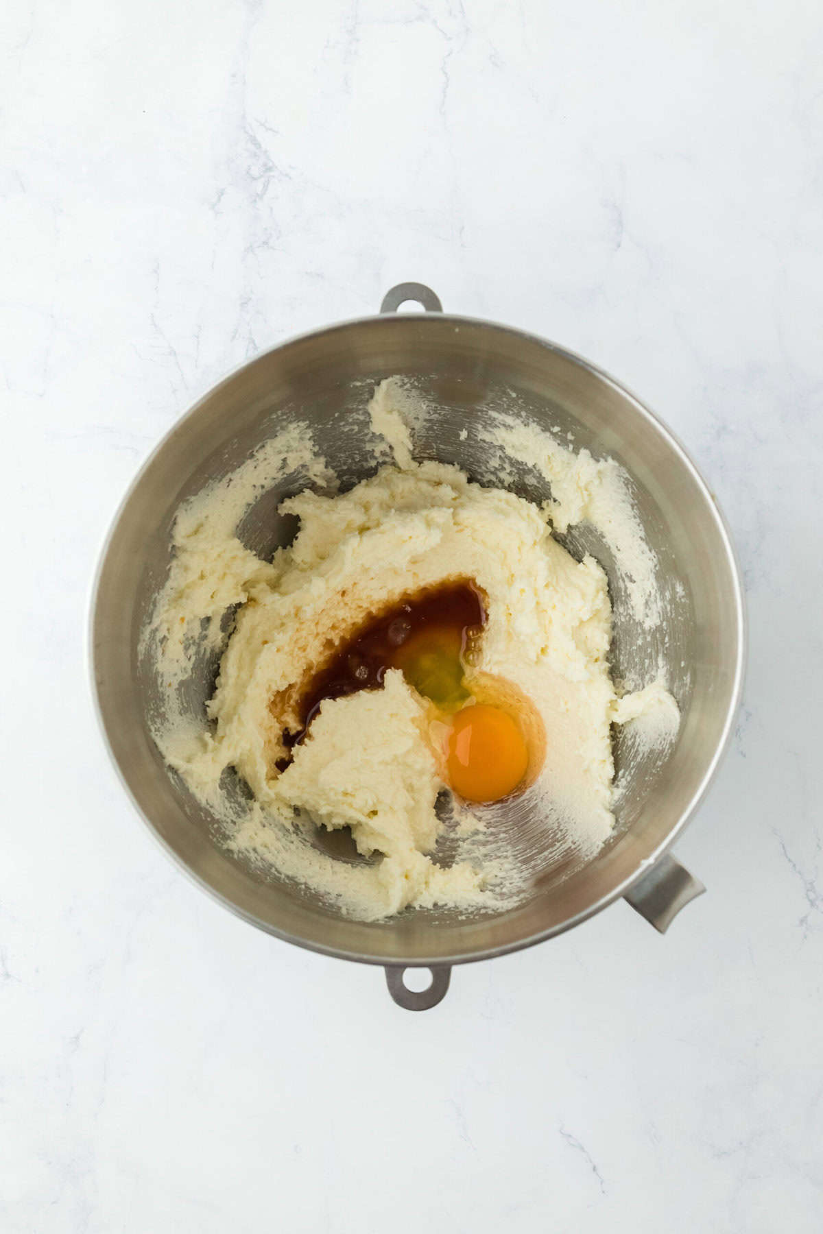 Creamed butter and sugar in a stand mixer bowl with egg and vanilla added on a white countertop.