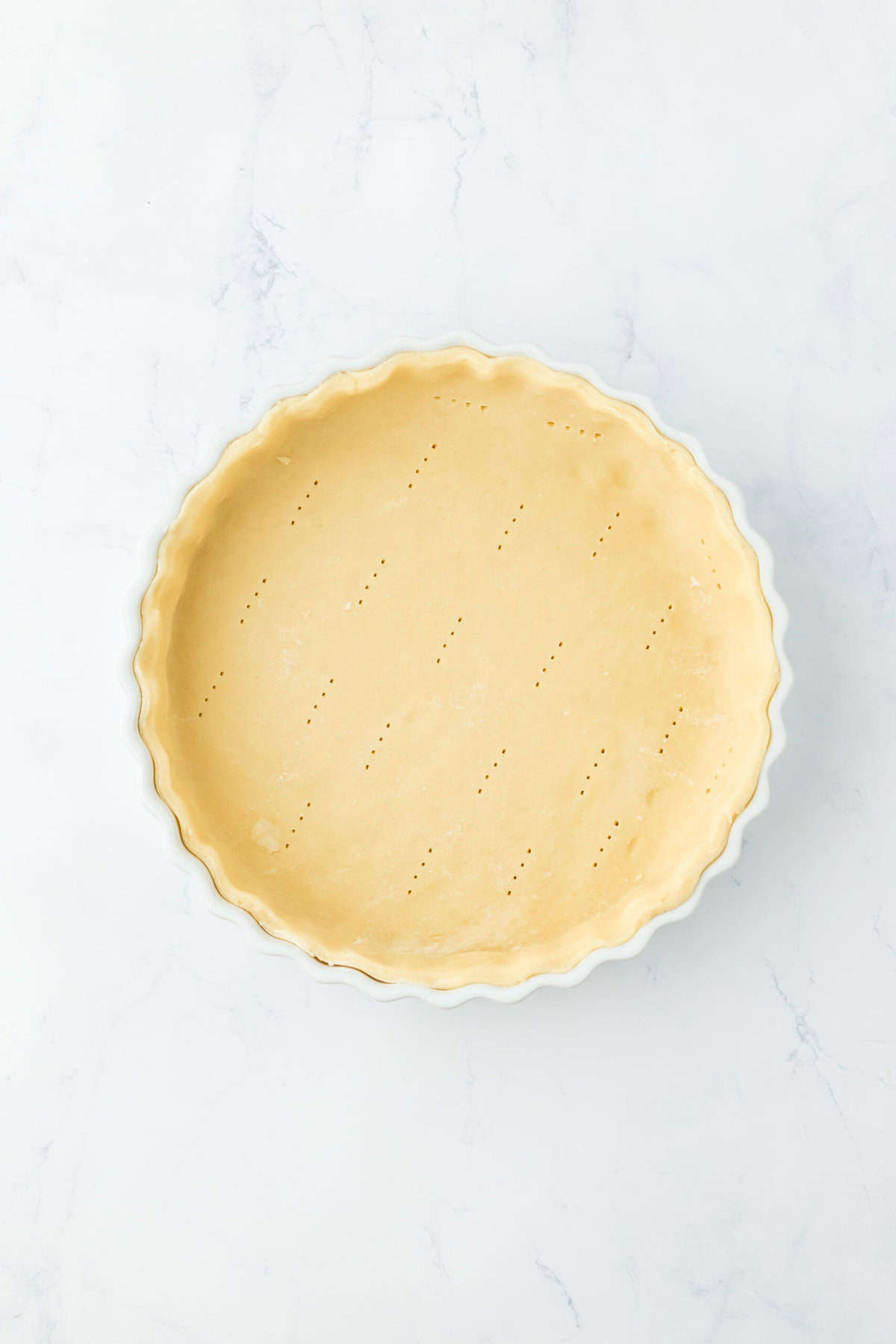 Pie dough added to a pie plate on white countertop.