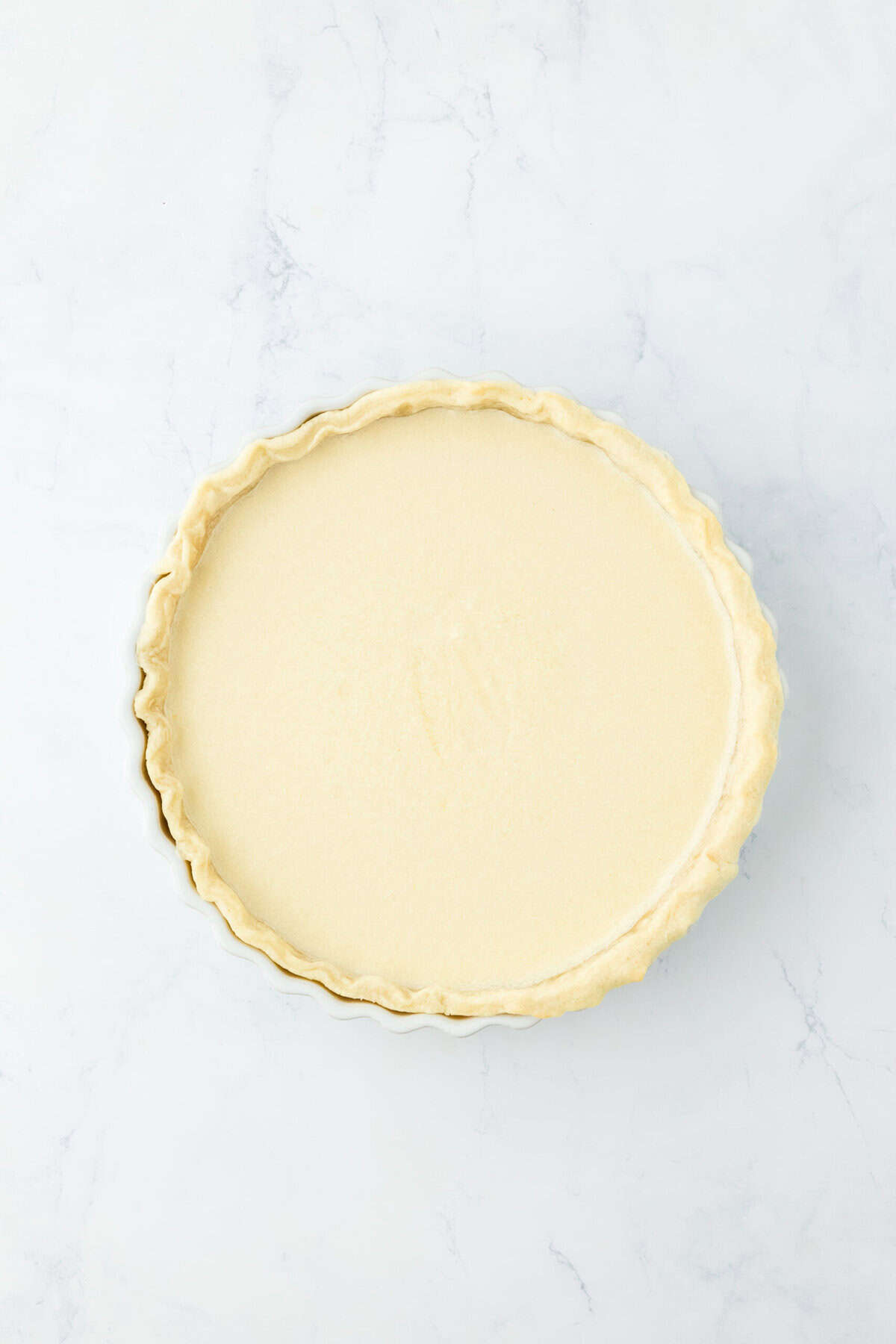 Buttermilk custard filling added to pie crust on white countertop.