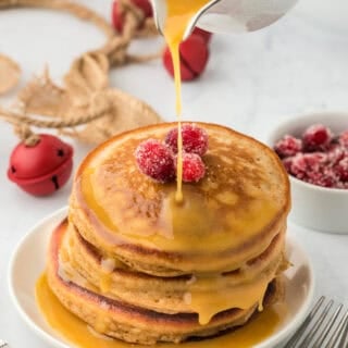 Perfect gingerbread pancakes in a stack on a white plate with syrup being drizzled on top