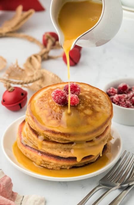 Perfect gingerbread pancakes in a stack on a white plate with syrup being drizzled on top