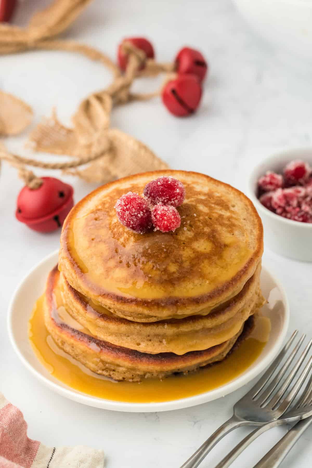 A stack of gingerbread pancakes recipe on a white plate with candied cranberries and syrup