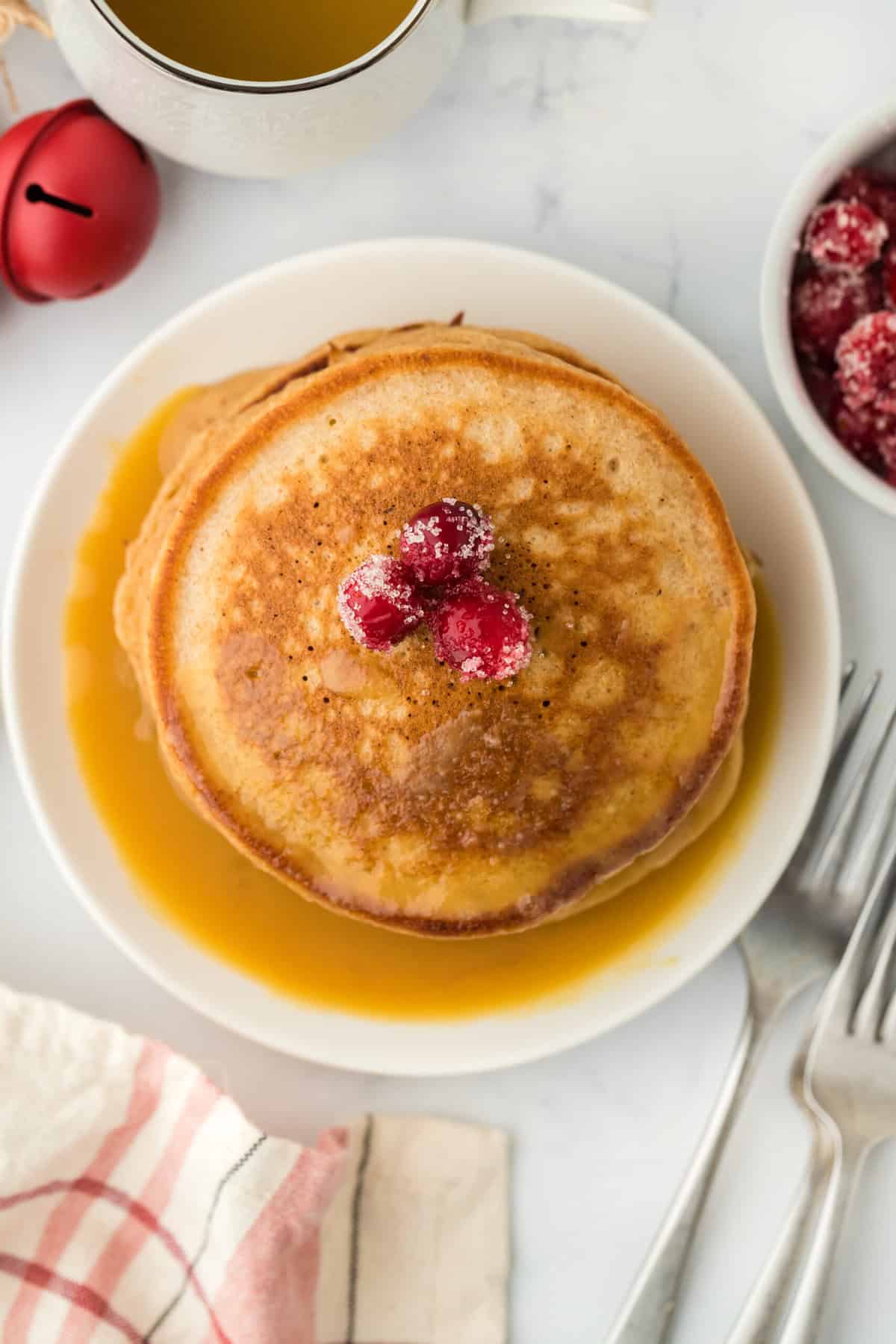 Gingerbread pancake recipe stacked on white plate with candied cranberries on white countertop