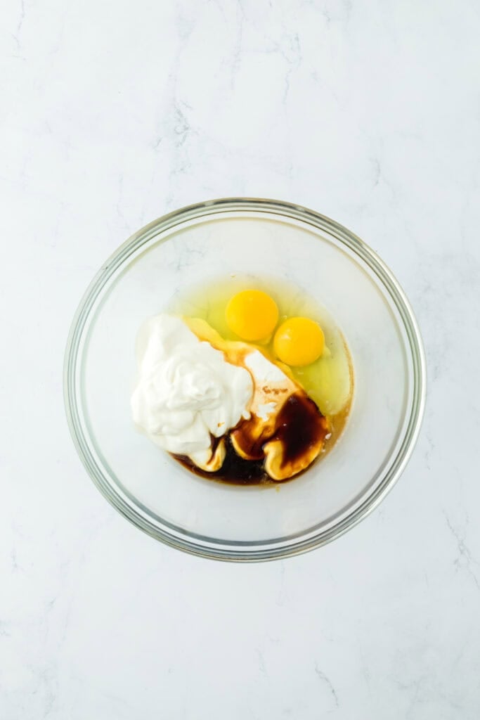 Sour cream, eggs, molasses, melted butter and vanilla in a glass bowl on white countertop