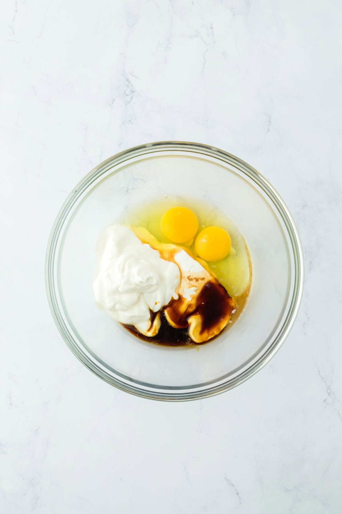 Sour cream, eggs, molasses, melted butter and vanilla in a glass bowl on white countertop