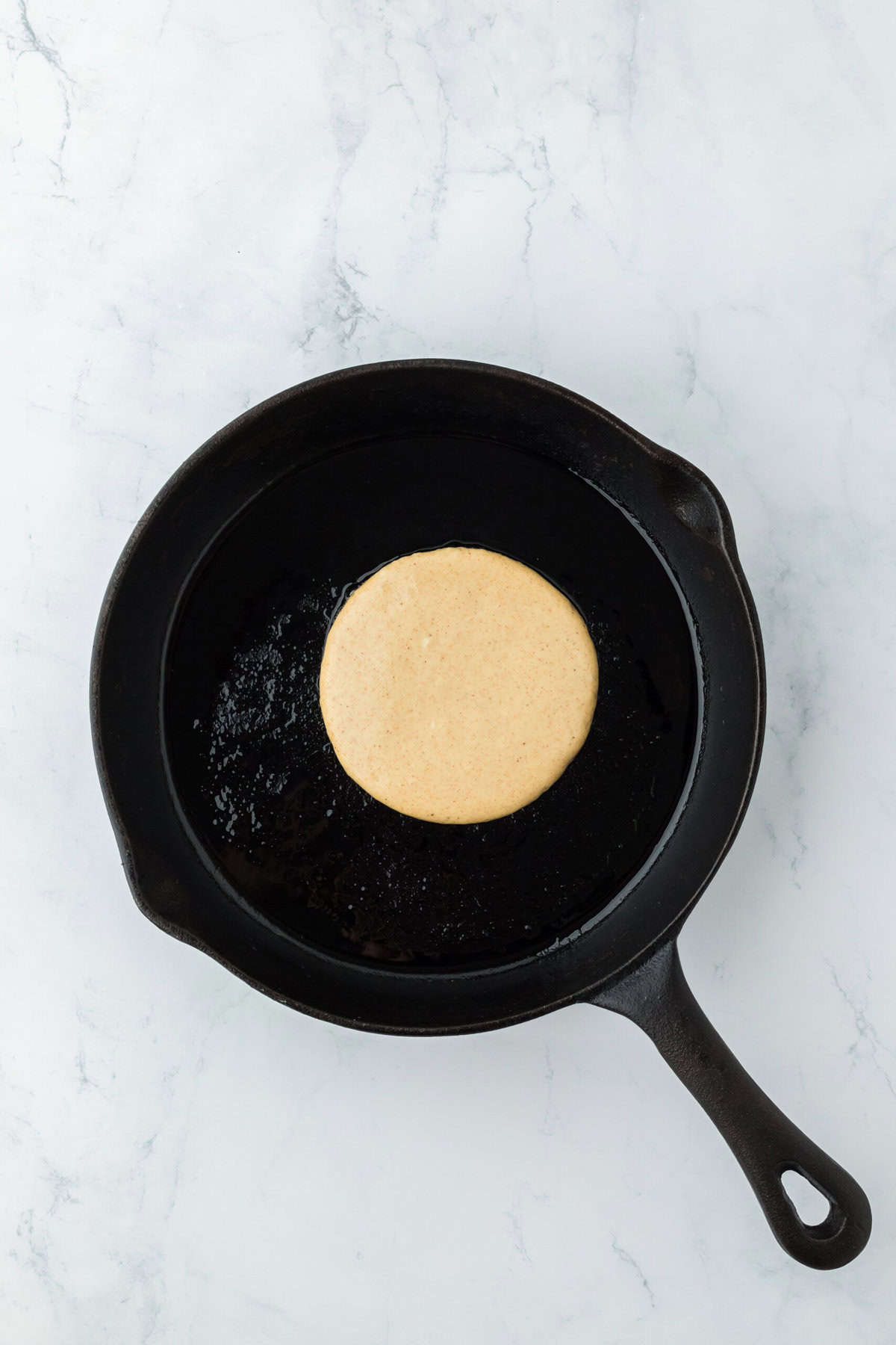 Cast iron skillet heated with a gingerbread pancake in the center frying on white countertop