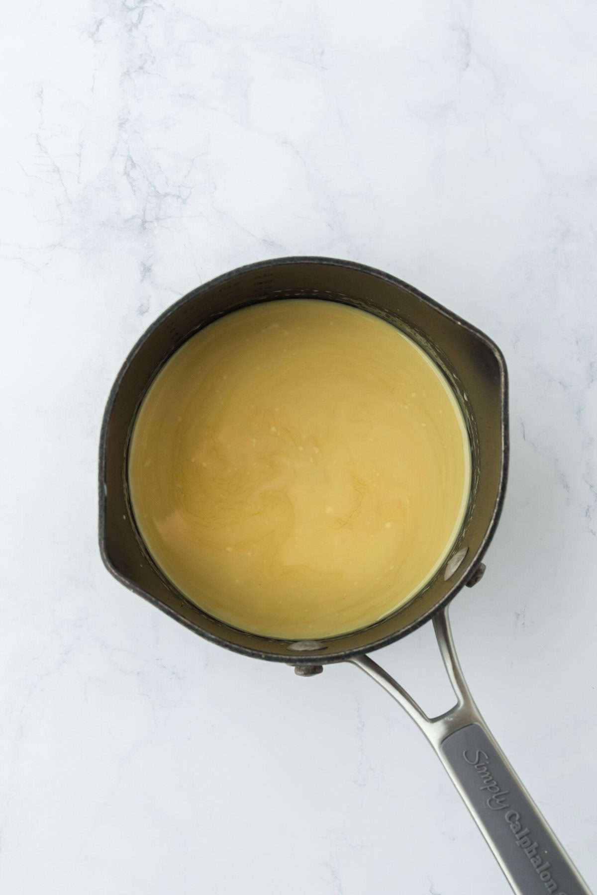 Eggnog and syrup added to a saucepan on white countertop