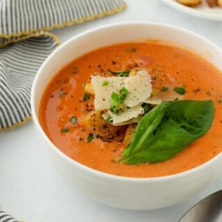 Homemade tomato basil soup garnished with fresh basil, cheese and croutons, presented in a bowl with a spoon beside it