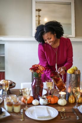 Jocelyn Delk Adams sharing Friendsgiving ideas and pouring from orange pitcher over tablescape