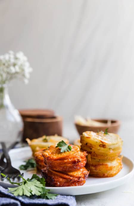 Sweet Potato Stacks and Yukon Gold Potato Stacks on white plate with parsley garnish and white flowers background