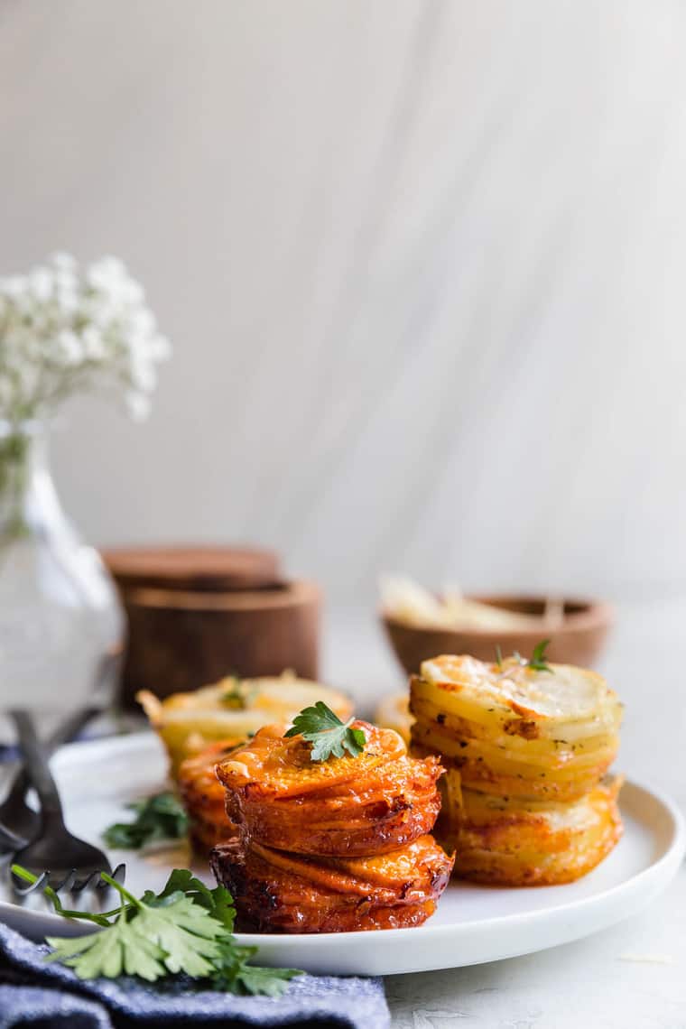 Sweet Potato Stacks and Yukon Gold Potato Stacks on white plate with parsley garnish and white flowers background