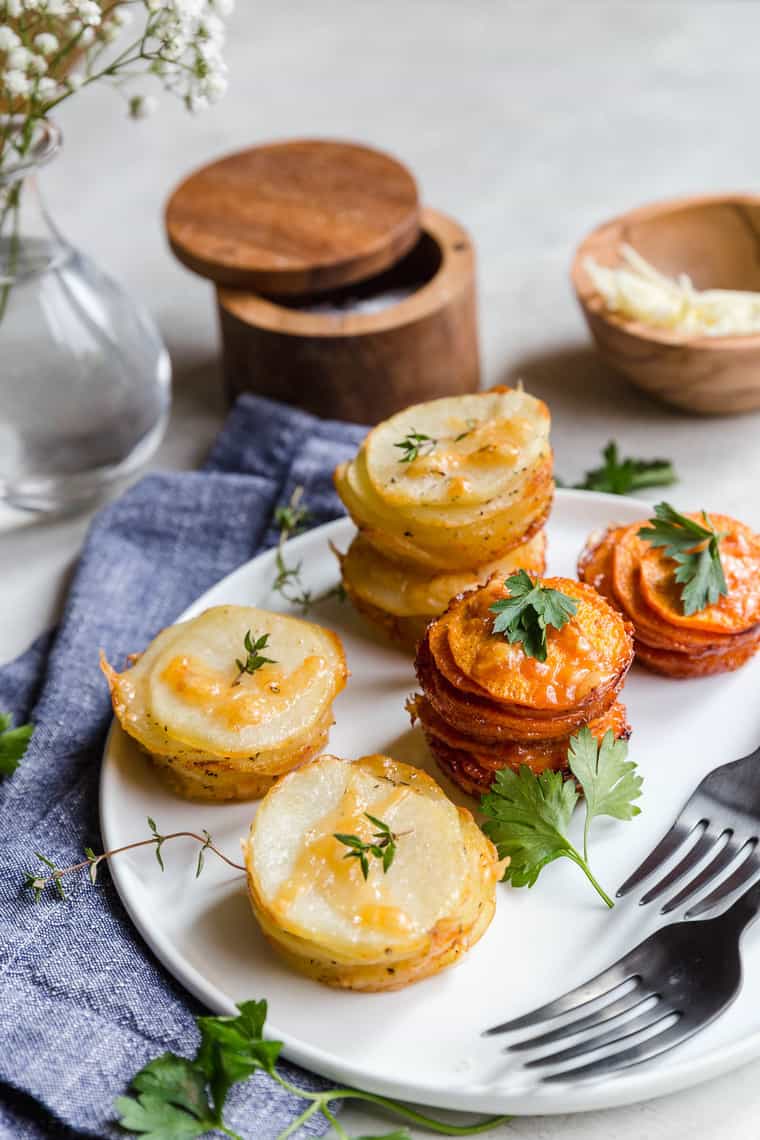 Sweet Potato Stacks and Yukon Gold Potato Stacks on white plate with parsley garnish and white flowers background with blue napkin