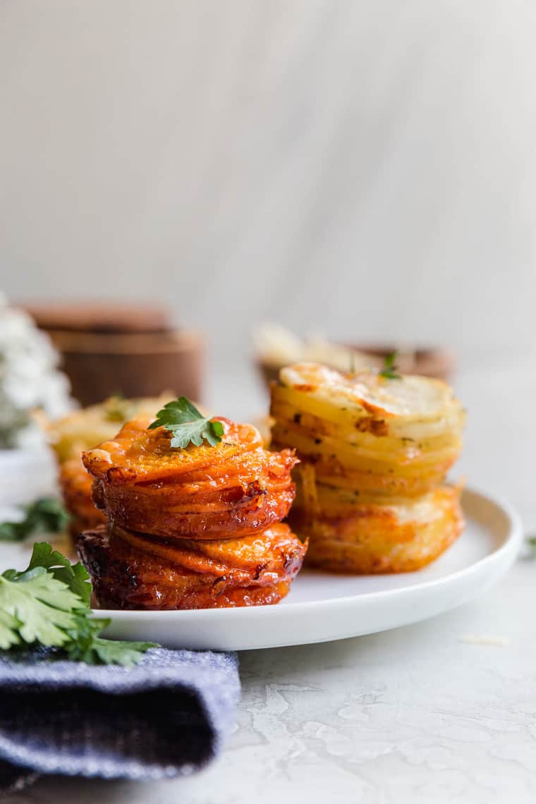 Close up of Sweet Potato Stacks and Yukon Gold Potato Stacks on white plate with parsley garnish and white flowers background