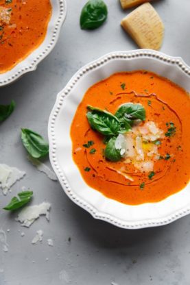 Whole Tomato Basil Soup Recipe in white bowl garnished with fresh basil, oil and shredded parmesan cheese