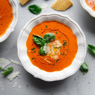 Tomato Soup in white bowl garnished with fresh basil, oil and shredded parmesan cheese