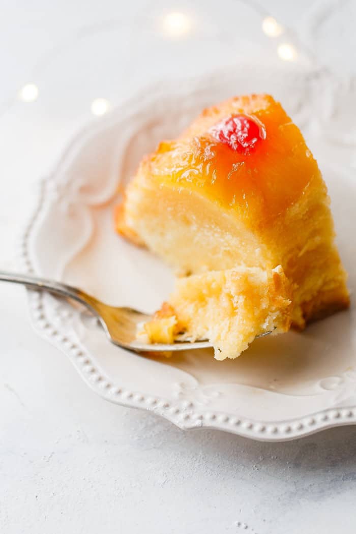 A slice of pineapple rum cake with fork on white plate