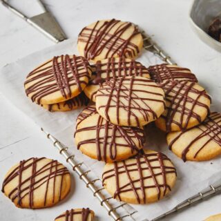 Overhead of a dozen chocolate drizzled shortbread cookies on a silver tray against white background