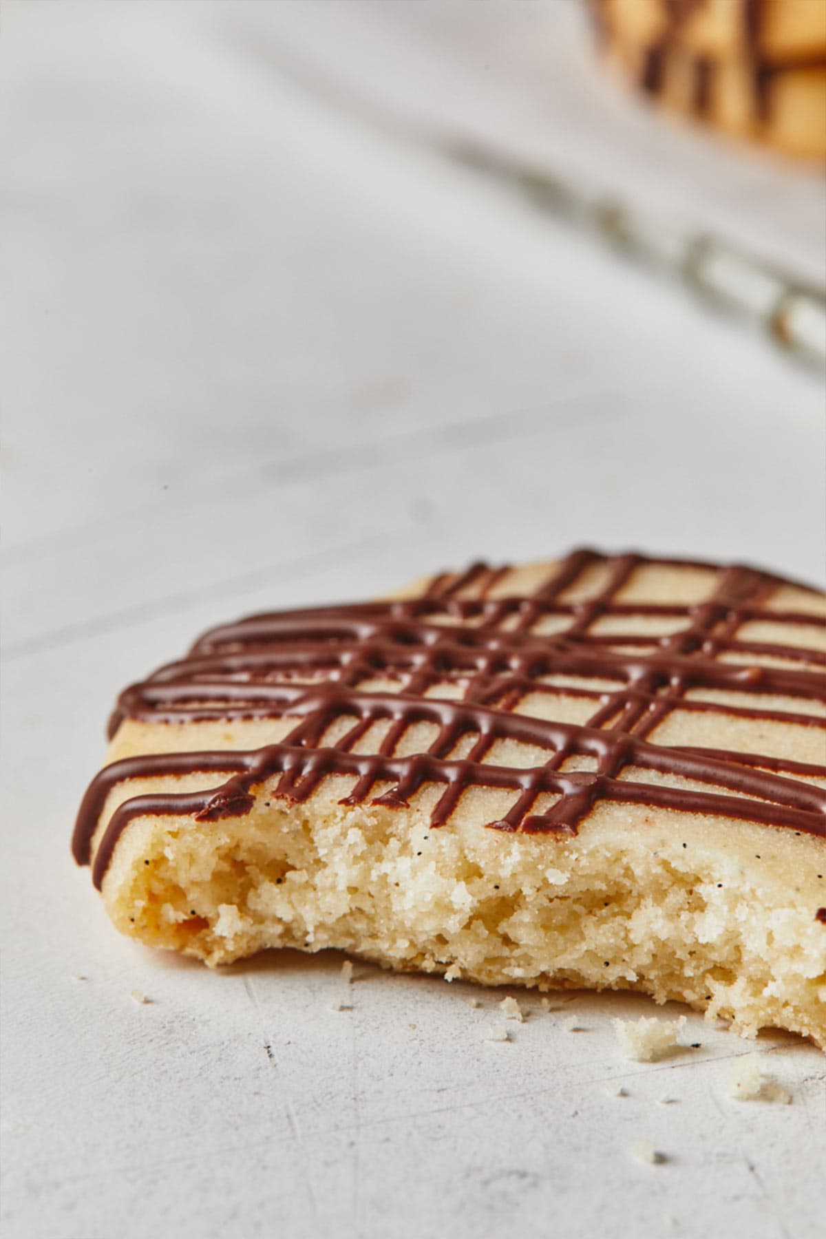 Close up shot of broken shortbread cookie with chocolate drizzle against white background.