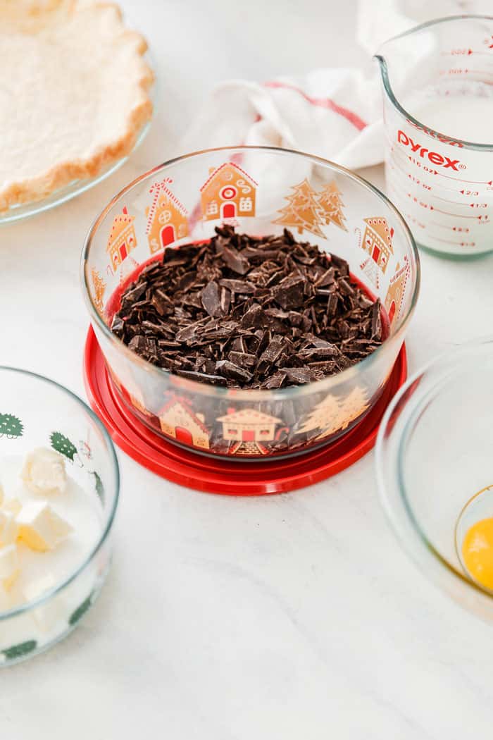 Chocolate pieces in holiday glass pyrex bowl with ingredients for chocolate pie in other bowls