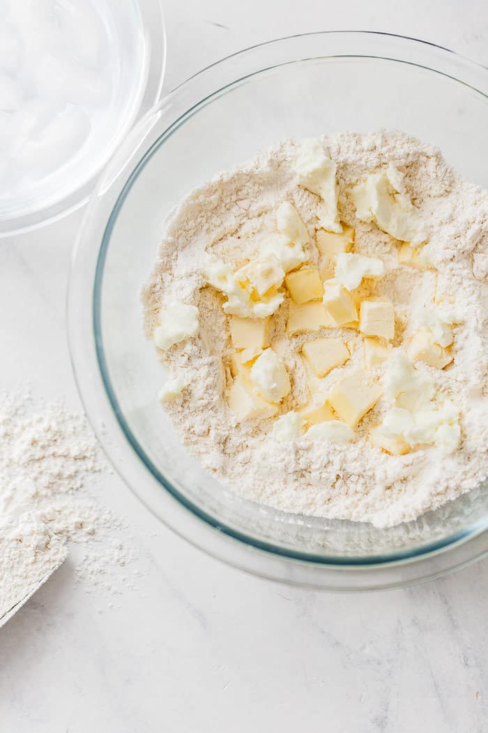 Cold butter in flour mixture preparing to make pie dough in glass bowl against white background