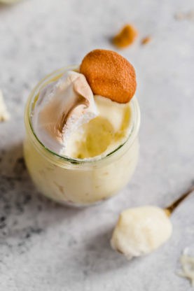 Overhead shot of banana pudding in a mini glass with nilla cookie and meringue with a spoon of some out