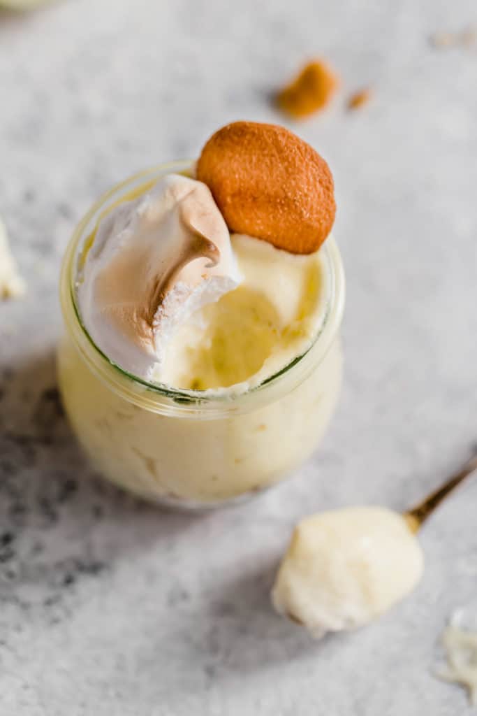 Overhead shot of one homemade banana pudding in a mini glass with nilla cookie and meringue with a spoon of some out
