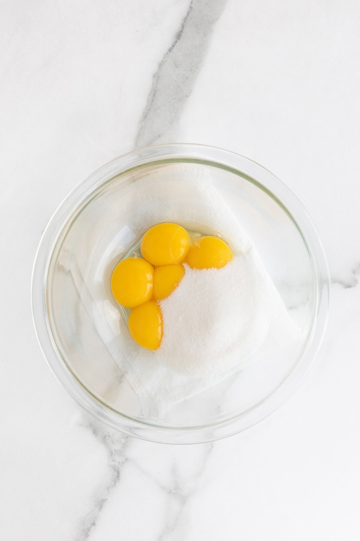 Eggs and sugar in a glass bowl on white countertop