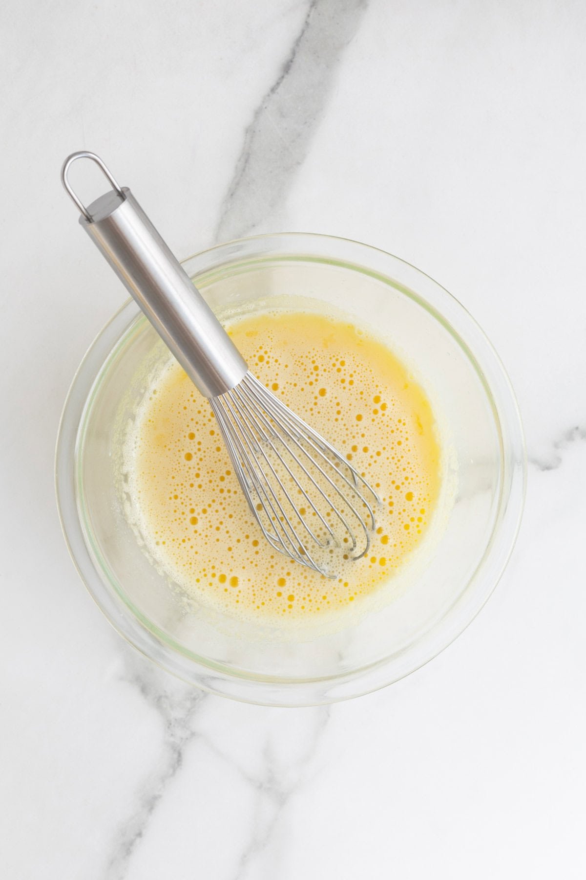 Egg yolks and hot milk whisk together in glass bowl