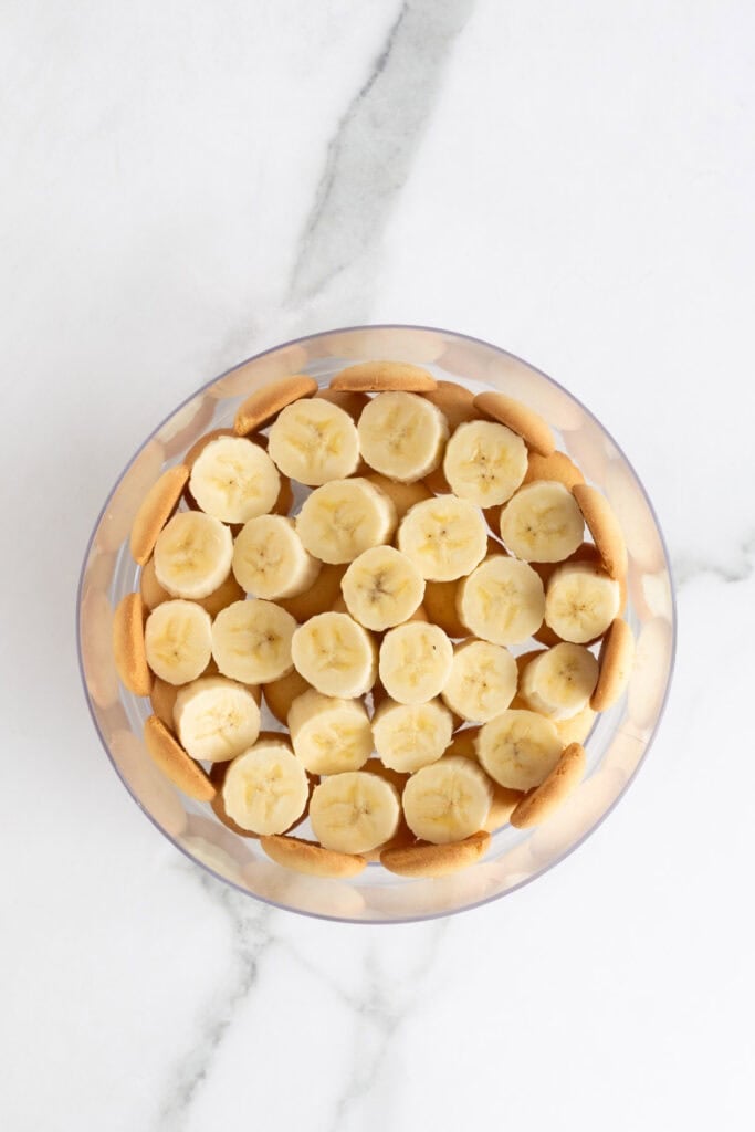 Banana slices added to the bottom of nilla wafers in a trifle bowl