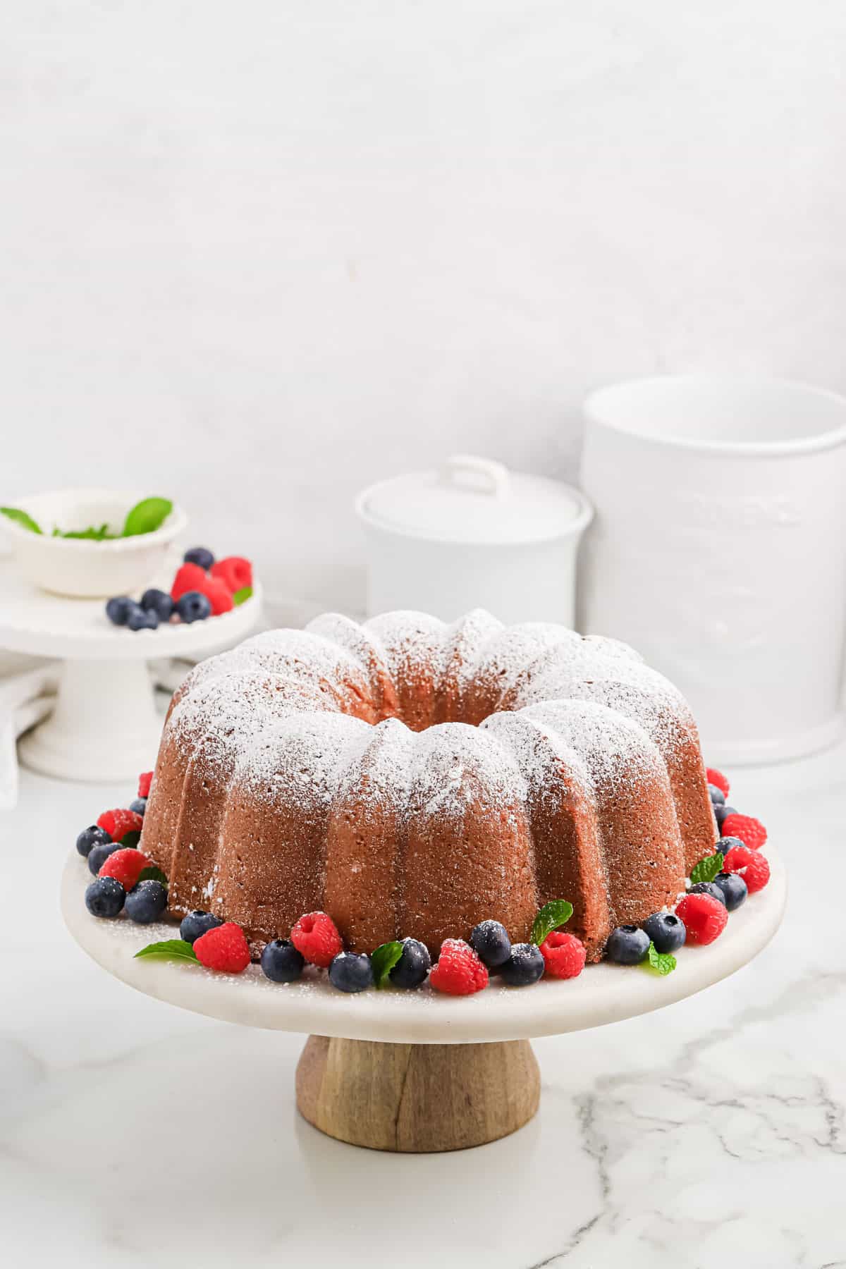 Cream cheese pound cake on a white cake stand with berries.