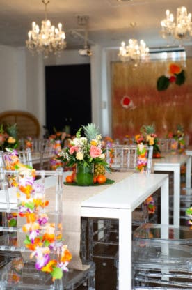 Shot of white tables and clear chairs with plastic leis hanging on them and Hawaiian themed table settings