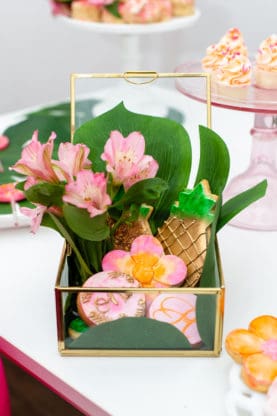 Birthday cookies in the shape of pineapples and flowers in a glass box display
