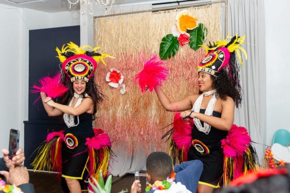 Two hula dancers dancing in front of a grass curtain