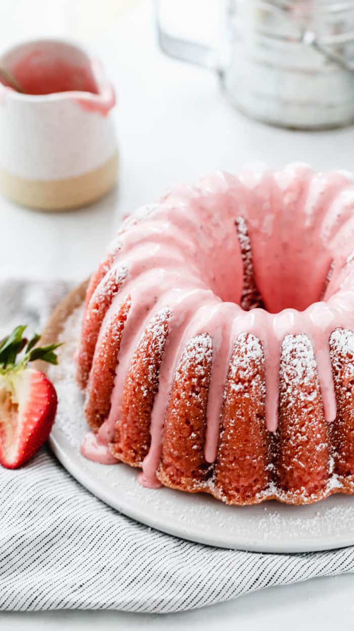 Close up on Fresh Strawberry Pound Cake sitting on a white cake plate with a container of strawberry glaze in the background