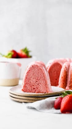 Strawberry Cake slice on white plate with the sliced cake in the background along with a bowl of fresh of strawberries