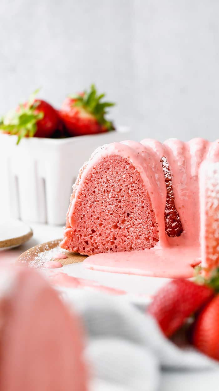 Delicious sliced Homemade Strawberry Cake with slices missing and a white basket of fresh strawberries in the background