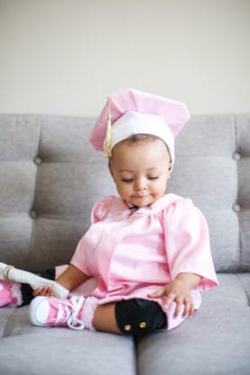 Baby Cakes Harmony sitting on couch wearing her pink graduation cap and gown