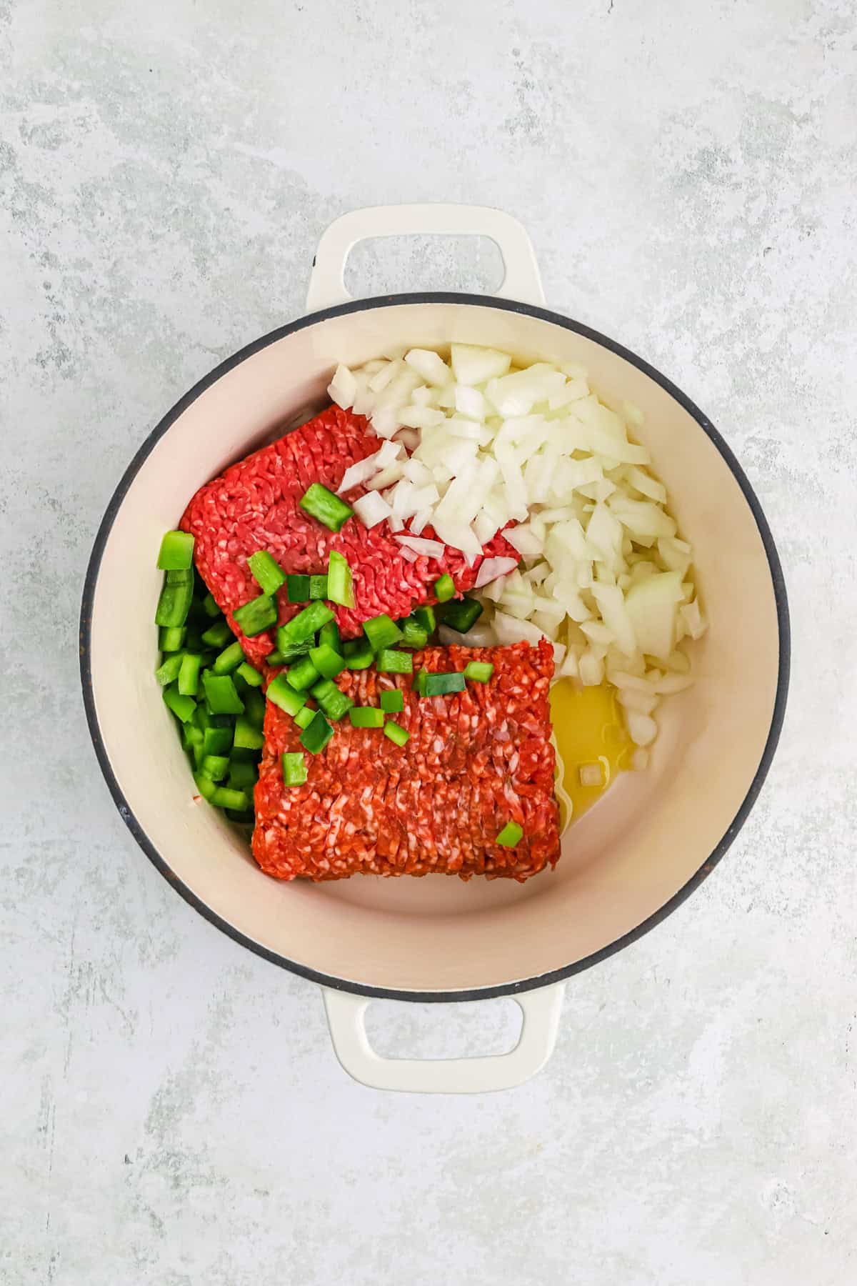 ground beef and sausage in a large pot with veggies and olive oil on gray background