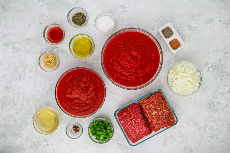 Ingredients to make homemade spaghetti sauce in clear bowls on gray background