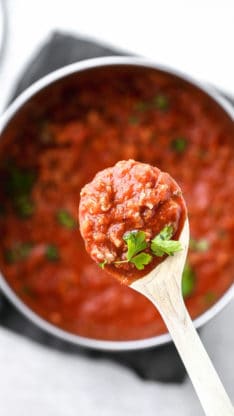 Large spoon of homemade Southern spaghetti sauce with the entire pot full of the sauce in the background